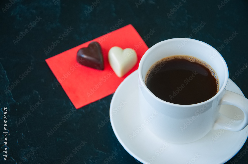 Cup of strong coffee and heart shaped dark and white chocolates on a black background.