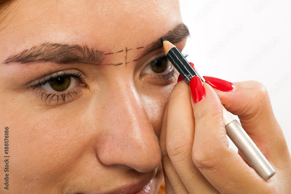 The procedure for eyebrow correction in the beauty salon. The make-up artist penciled an ideal eyebrow shape on a young red-haired woman  on a white background