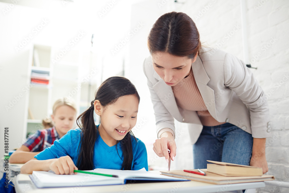 Teacher checking home assignment of cute schoolgirl and reading her notes in copybook Teacher checking home assignment of cute schoolgirl and reading her notes in copybook