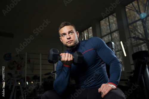 Young man holding dumbbell and exercising during workout in gym
