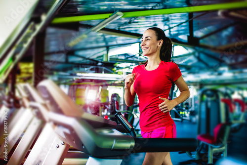 Confidence and grace in every movement. A beautiful smiling sportswoman in colorful sportswear on a treadmill in the gym.