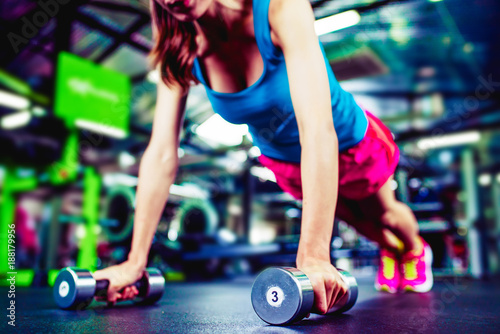 Girl with dumbbells. Modern young brunette warming up and doing some push ups a the gym