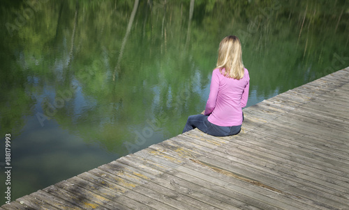 Woman sitting on the edge of a wooden pier and observing fish in water. © robsonphoto