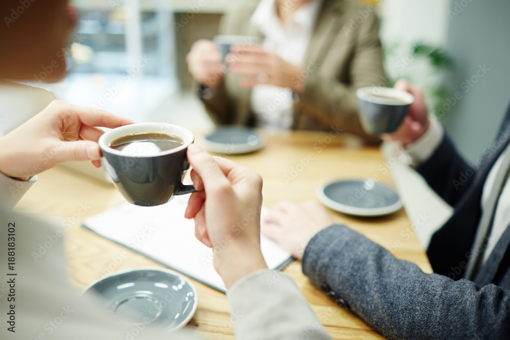 Cup of black tea or coffee held by businesswoman during coffee-break with colleagues