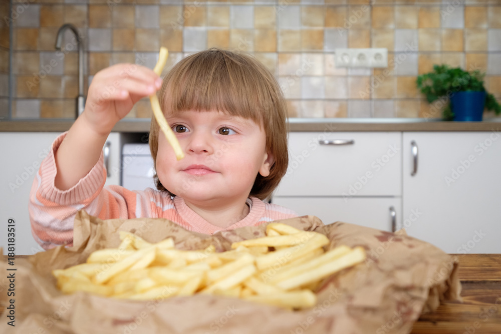 Cute little baby girl enjoying french fries on kitchen Cute little baby girl enjoying french fries on kitchen
