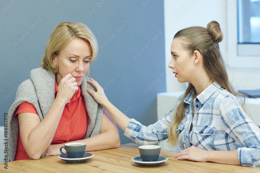 Young colleague comforting mature woman while sitting in cafe by cup of tea