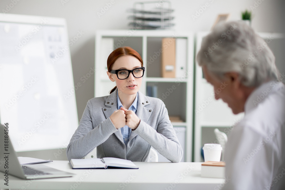 Young employee sitting by desk and making report to her director or sharing her business ideas Young employee sitting by desk and making report to her director or sharing her business ideas