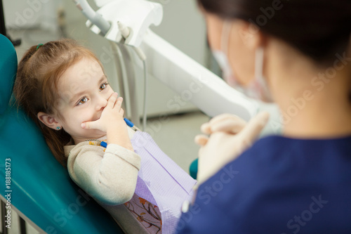 Child closes mouth with hand and sits in dentist chair