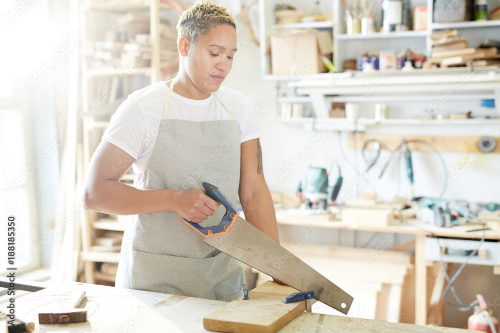 Female carpenter with handsaw working with wooden board in workshop Female carpenter with handsaw working with wooden board in workshop