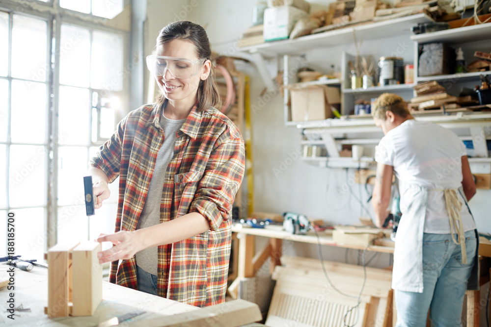 Female carpenter hammering nails into wooden box while standing by workbench Female carpenter hammering nails into wooden box while standing by workbench