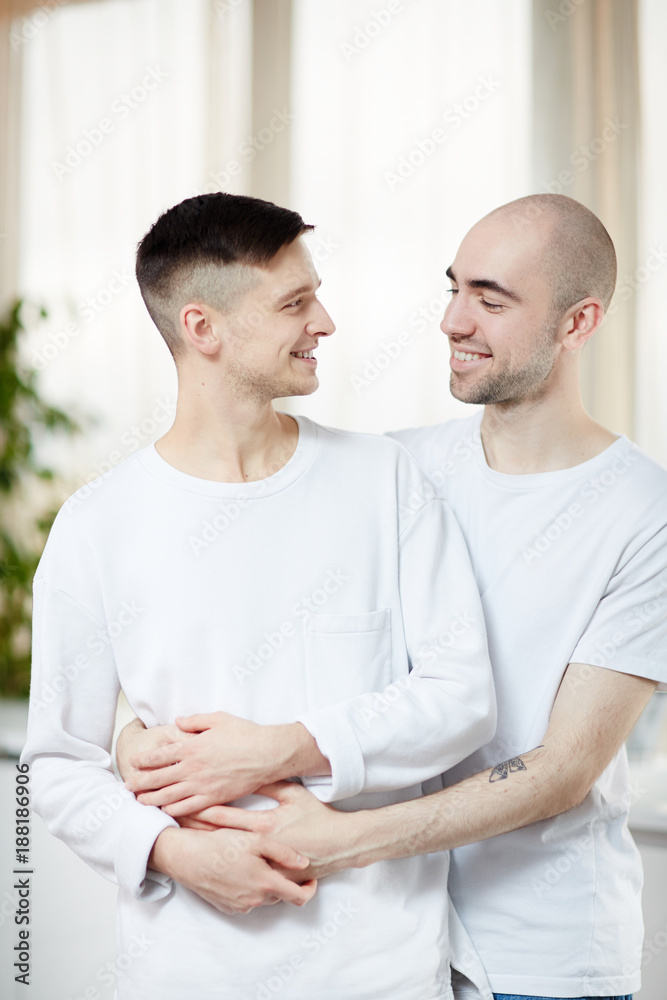 Young gay partners in white T-shirts looking at one another in embrace Young gay partners in white T-shirts looking at one another in embrace