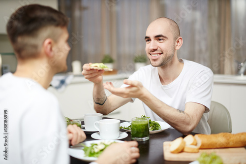 Happy young man giving healthy sandwich to his partner during breakfast