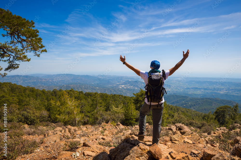 Obraz premium Traveler with open arms stands on the cliff, among green hills