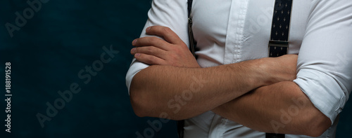 Closeup of Hands of an unidentified strong man in formal attire with suspenders folded on chest on blue grunge background