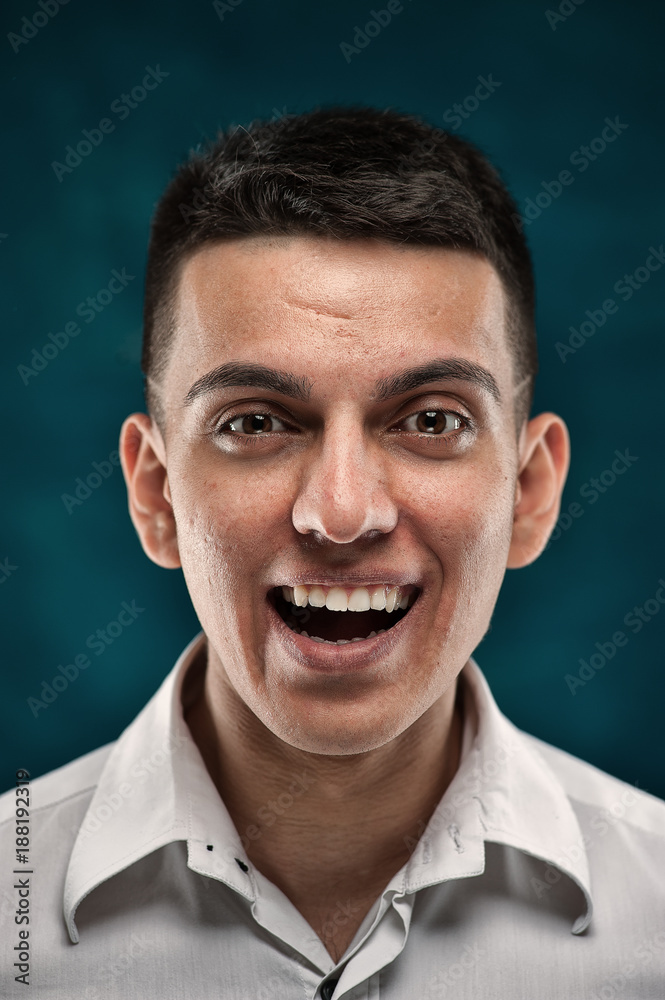 Close-up portrait of young handsome man showing happy emotions on dark blue background Close-up portrait of young handsome man showing happy emotions on dark blue background
