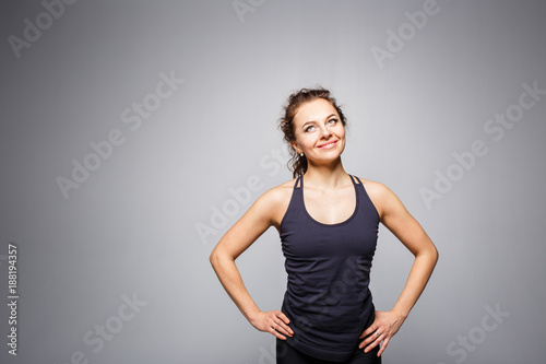 Cheerful young fitness woman standing against grey background with copy space