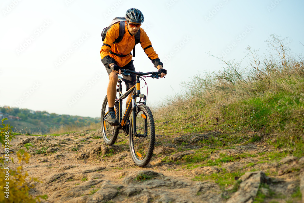 Cyclist in Orange Riding the Mountain Bike on the Autumn Rocky Trail. Extreme Sport and Enduro Biking Concept. Cyclist in Orange Riding the Mountain Bike on the Autumn Rocky Trail. Extreme Sport and Enduro Biking Concept.