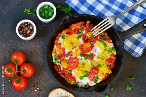 Eggs with tomatoes, pepper and green peas in a frying pan on a concrete background.