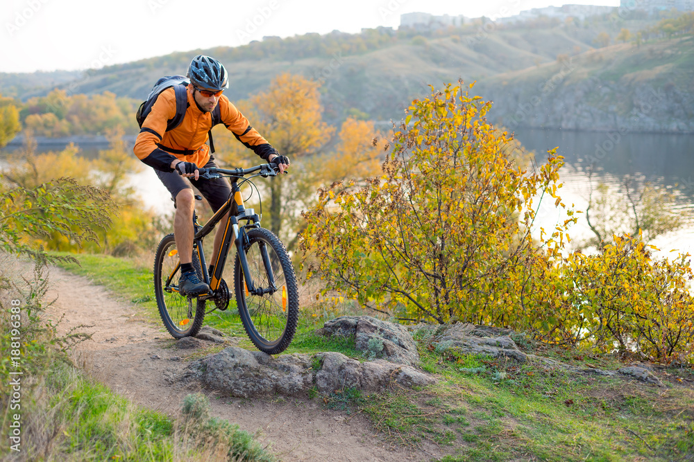 Naklejka premium Cyclist in Orange Riding the Mountain Bike on the Autumn Rocky Trail. Extreme Sport and Enduro Biking Concept.