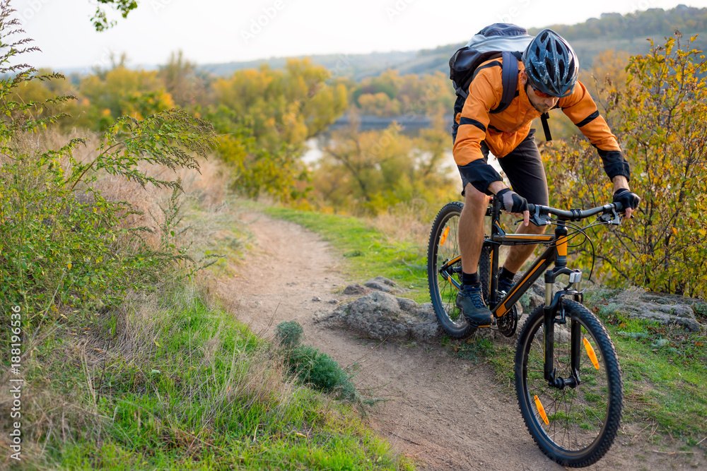 Cyclist in Orange Riding the Mountain Bike on the Autumn Rocky Trail. Extreme Sport and Enduro Biking Concept. Cyclist in Orange Riding the Mountain Bike on the Autumn Rocky Trail. Extreme Sport and Enduro Biking Concept.