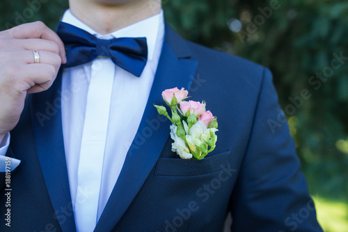 Stylish groom in blue jacket, white shirt with white and pink boutonniere. A golden wedding ring on a groom’s finger.