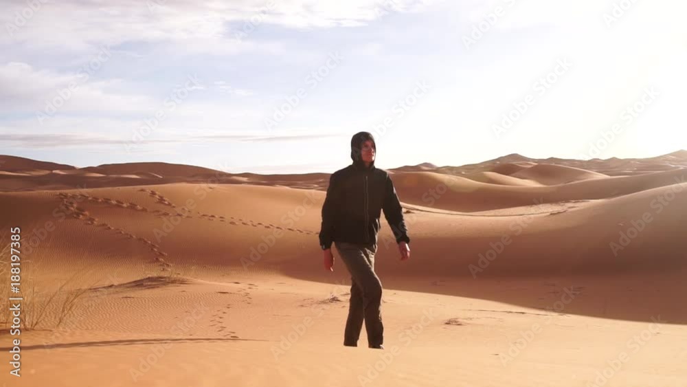 young man walking up sand dunes during a sunny day; Erg Chebbi, Maroc young man walking up sand dunes during a sunny day; Erg Chebbi, Maroc