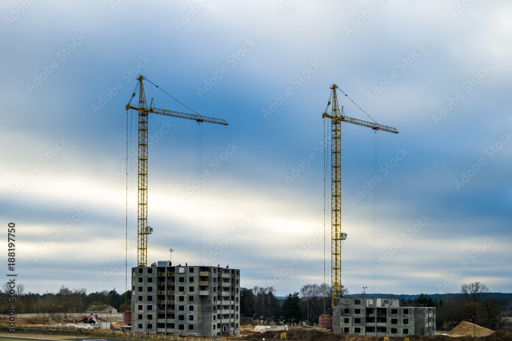 Silhouette tower cranes and unfinished multi-storey high buildings under construction in cloudy day