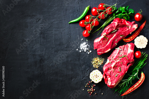 Raw meat, beef steak on a stone cutting board with rosemary, spices, salt, oil, cherry tomatoes, hot pepper and herbs