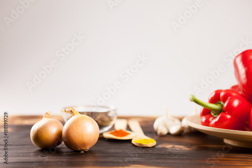 Onions with sweet red pepper on a wooden plate over gray background