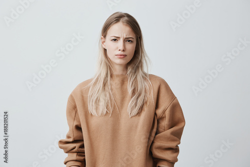 Canvas Print Dissatisfied blonde young woman wearing long sleeved sweater frowning face, looking angrily at camera, being displeased with her husband`s words