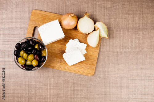 Feta cheese on a wooden baord next to cut onions and a glass bowl of olives photo