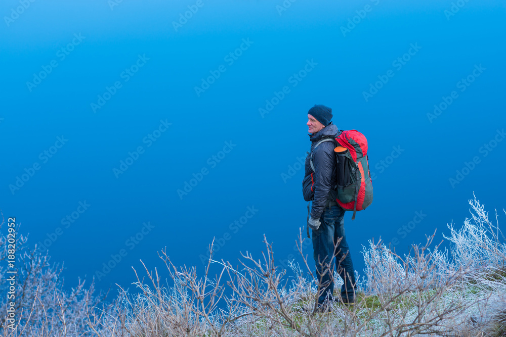 Traveler is standing on a hill by the river, among the grass in frost