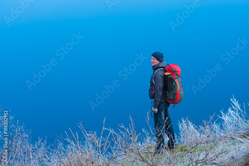 Traveler is standing on a hill by the river, among the grass in frost