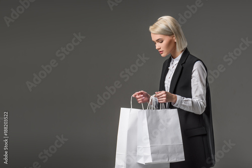 side view of young woman with shopping bags isolated on grey