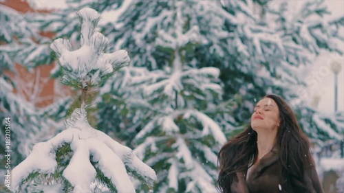 Close-up of Brunette woman throwing snow in air in winter holidays. Fashionable sexy pretty rich woman or glamour model girl with beautiful long hair in waist coat of brown fur in cold winter day