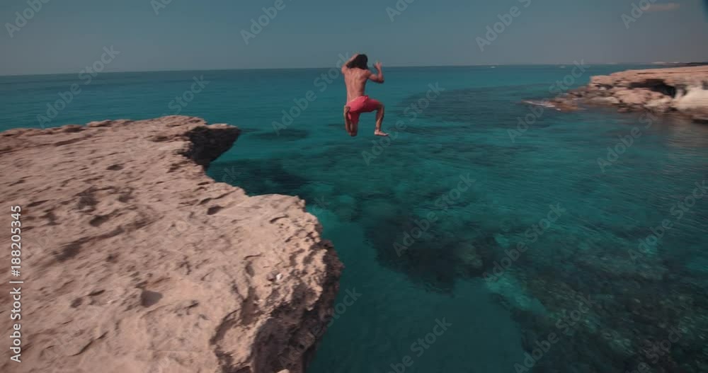 Young man jumping off cliff and diving into sea Young man jumping off cliff and diving into sea