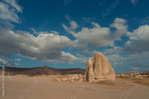 panorama of a desert valley with a large stone and floating clouds