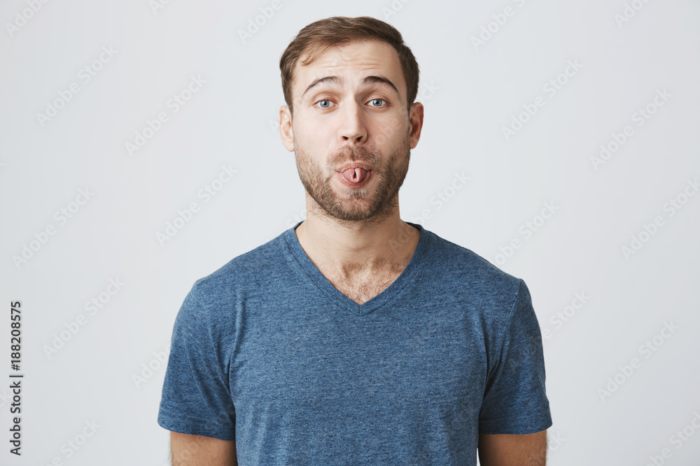 Gloomy young male with beard showing his digust and distaste having gloomy expression demonstrating tongue refusing to do something. Making faces handsome man with rejecting guilt isolated on gray Gloomy young male with beard showing his digust and distaste having gloomy expression demonstrating tongue refusing to do something. Making faces handsome man with rejecting guilt isolated on gray