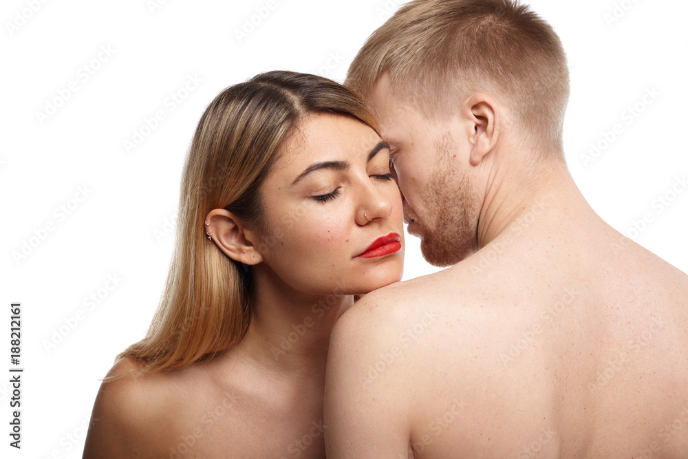 Cropped shot of beautiful naked couple: woman with ring nose and red lips closing eyes as she inhales body odor of her unrecognizable unshaven partner who is standing with his back to camera Cropped shot of beautiful naked couple: woman with ring nose and red lips closing eyes as she inhales body odor of her unrecognizable unshaven partner who is standing with his back to camera
