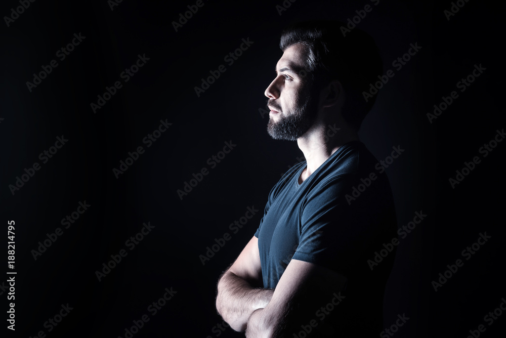 Half face. Pleasant nice handsome man standing cross handed and looking in front of him while being half face