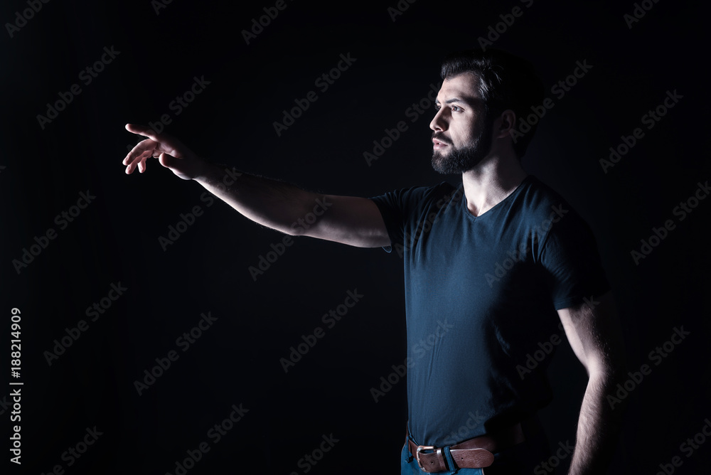 Over there. Nice pleasant handsome mans standing against black background and pointing with his hand while seeing something interesting Over there. Nice pleasant handsome mans standing against black background and pointing with his hand while seeing something interesting