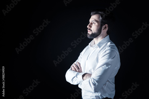 Handsome look. Serious nice bearded man standing cross handed and looking in front of him while being thoughtful