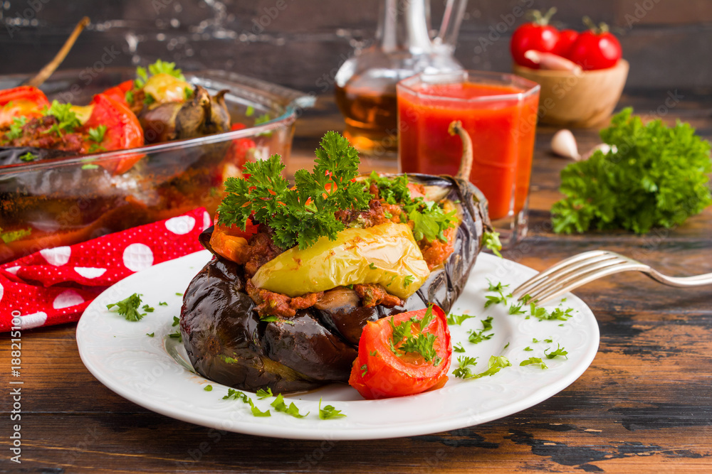 Eggplants stuffed with minced meat and cooked with fresh tomatoes and bell peppers on white plate and in baking dish on wooden rustic table. Eggplants stuffed with minced meat and cooked with fresh tomatoes and bell peppers on white plate and in baking dish on wooden rustic table.
