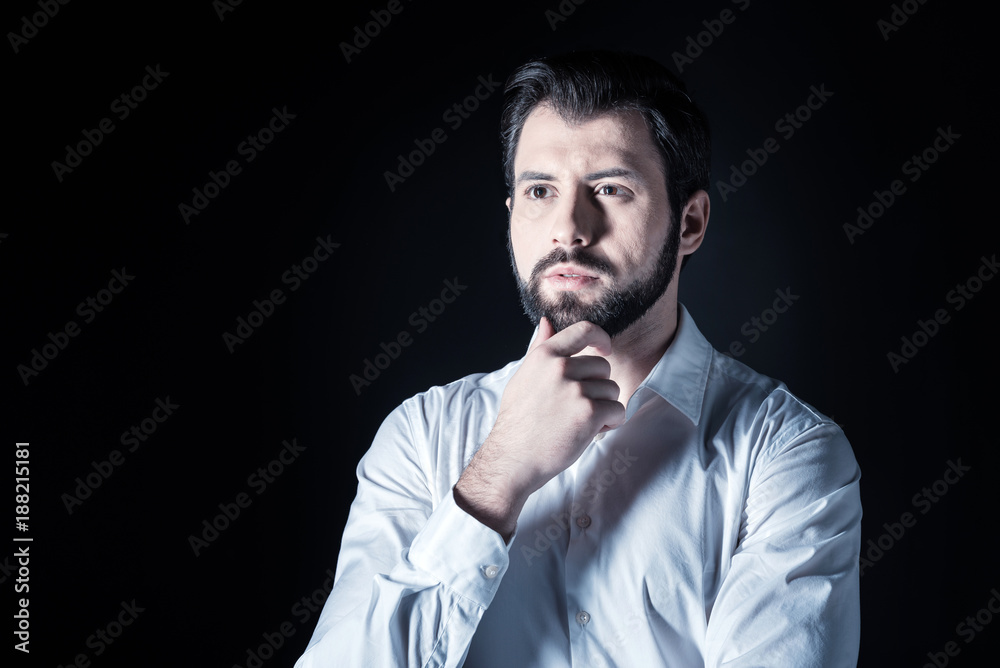 Being thoughtful. Pleasant nice handsome man looking in front of him and thinking while standing against black background