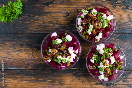 Healthy beet salad with cheese, parsley, walnuts and Greek yogurt in small glass bowls on the rustic wooden table, top view.