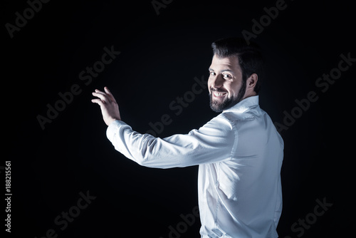 Sincere smile. Cheerful happy delighted man turning to you and smiling while touching the transparent screen