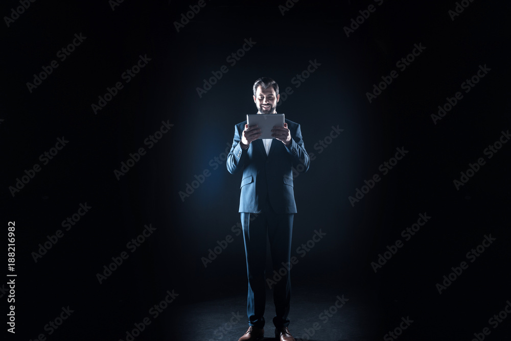 Device for work. Happy cheerful male businessman holding a tablet and smiling while looking at it Device for work. Happy cheerful male businessman holding a tablet and smiling while looking at it