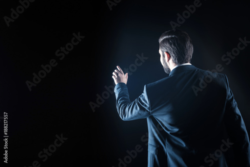 Professional tech. Nice smart handsome businessman standing against black background and touching the virtual screen while using modern technology