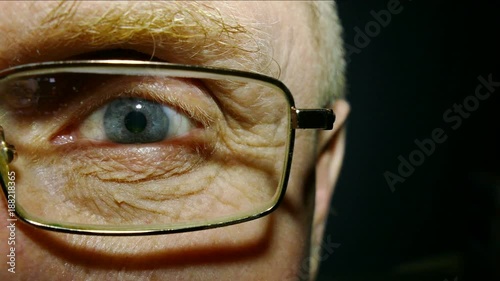 
An eye of the old man wearing spectacles with red capillaries. Macro
