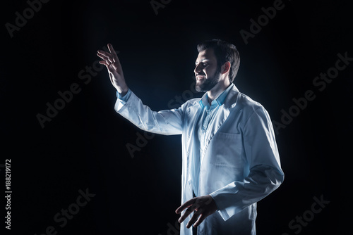Scientific technology. Happy nice smart scientist smiling and looking at the sensory screen while standing against black background